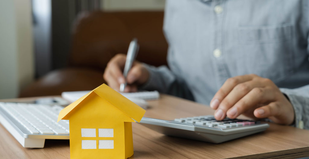 Personne en train d'effectuer des calculs de budget immobilier sur une feuille avec des chiffres visibles
